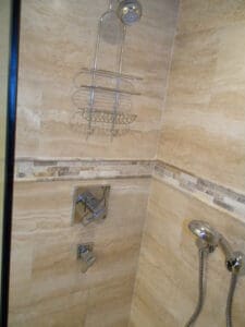 A bathroom with beige tile and a shower head.